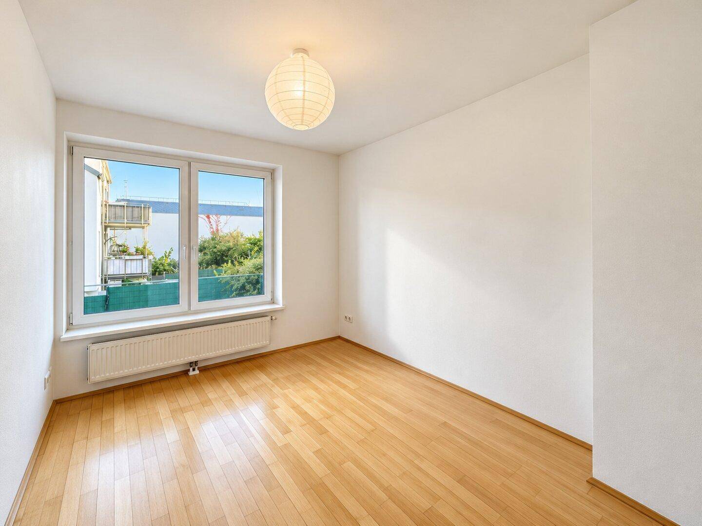 Freundliches Zimmer mit Holzboden und großem Fenster, das viel Tageslicht hereinlässt.