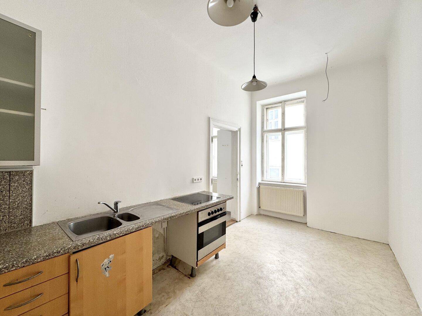 Einfache Küche mit Spüle, Herd und Fenster, bereit für eine Modernisierung.
