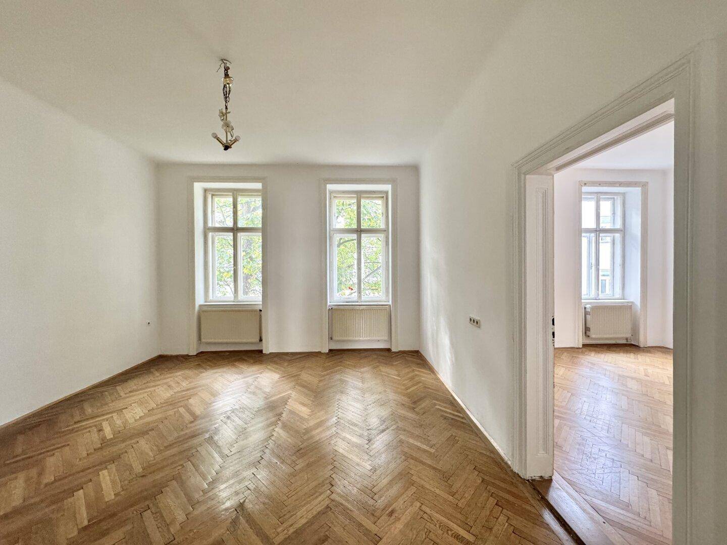 Geräumiges Zimmer mit klassischem Fischgrätparkett und Blick ins Grüne durch die Fenster.