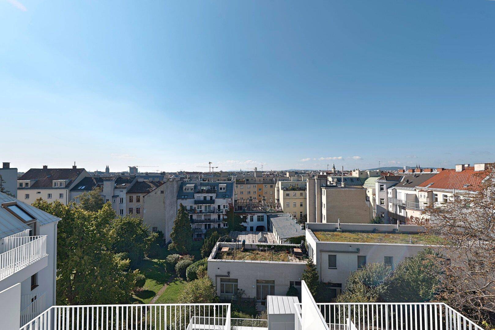 Weitläufiger Stadtblick über die Dächer Wiens mit viel Grün und klarem Himmel.