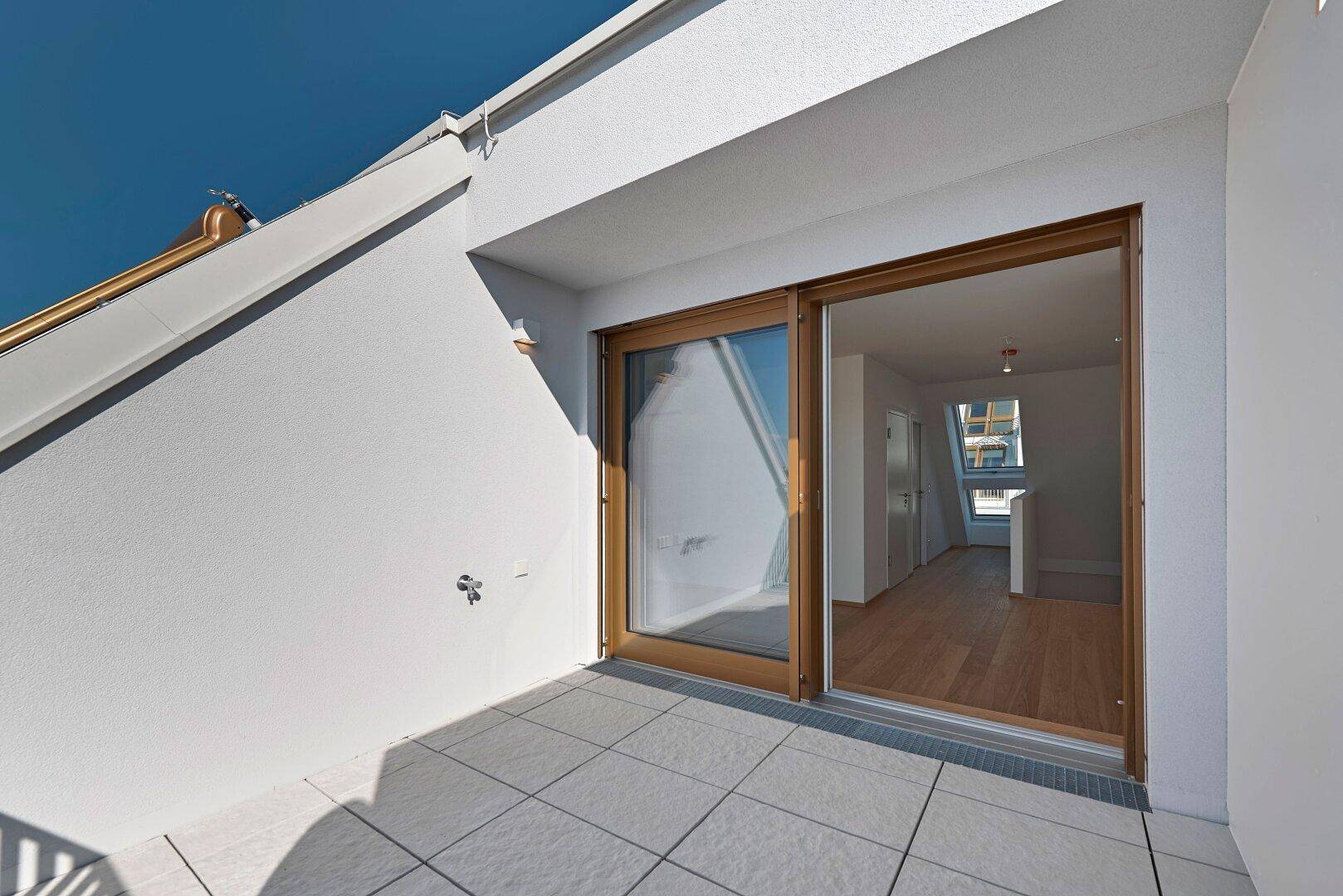 Kleiner Balkon mit Fliesenboden und Holztür, der Zugang zu einem hellen Innenraum bietet.