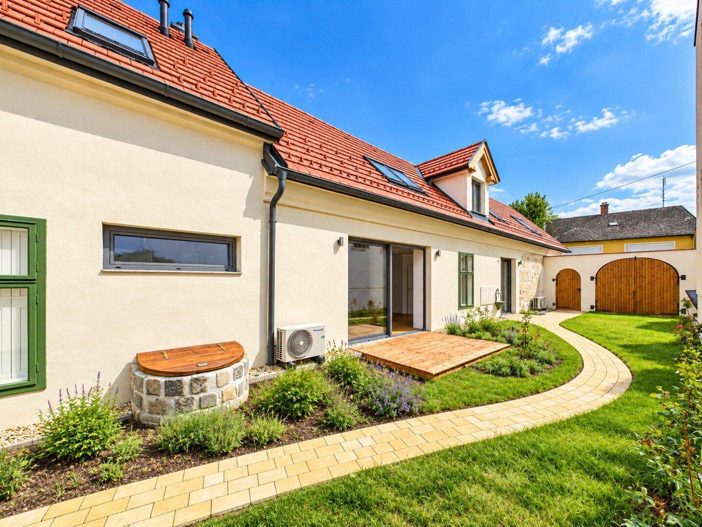 Gepflegter Gartenbereich neben dem Haus mit kleiner Holzterrasse und Steinbrunnen.