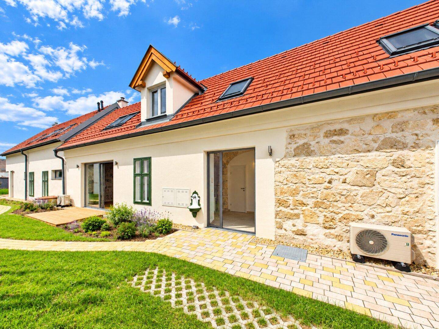 Lange Hausfassade mit Natursteinakzenten und einem gepflegten Gartenweg.