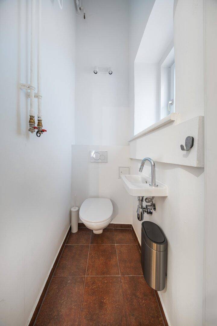 Modernes Gäste-WC mit Terrakotta-Fliesen, wandhängender Toilette und kleinem Handwaschbecken.