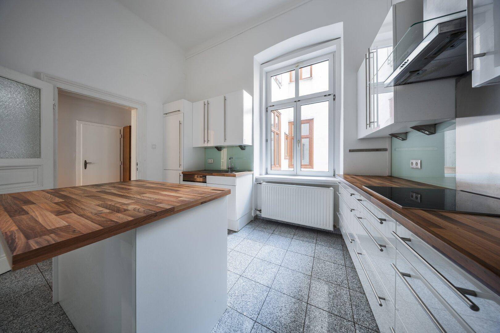 Moderne Küche mit weißen Schränken, Holzarbeitsplatte, Kücheninsel und Fliesenboden.
