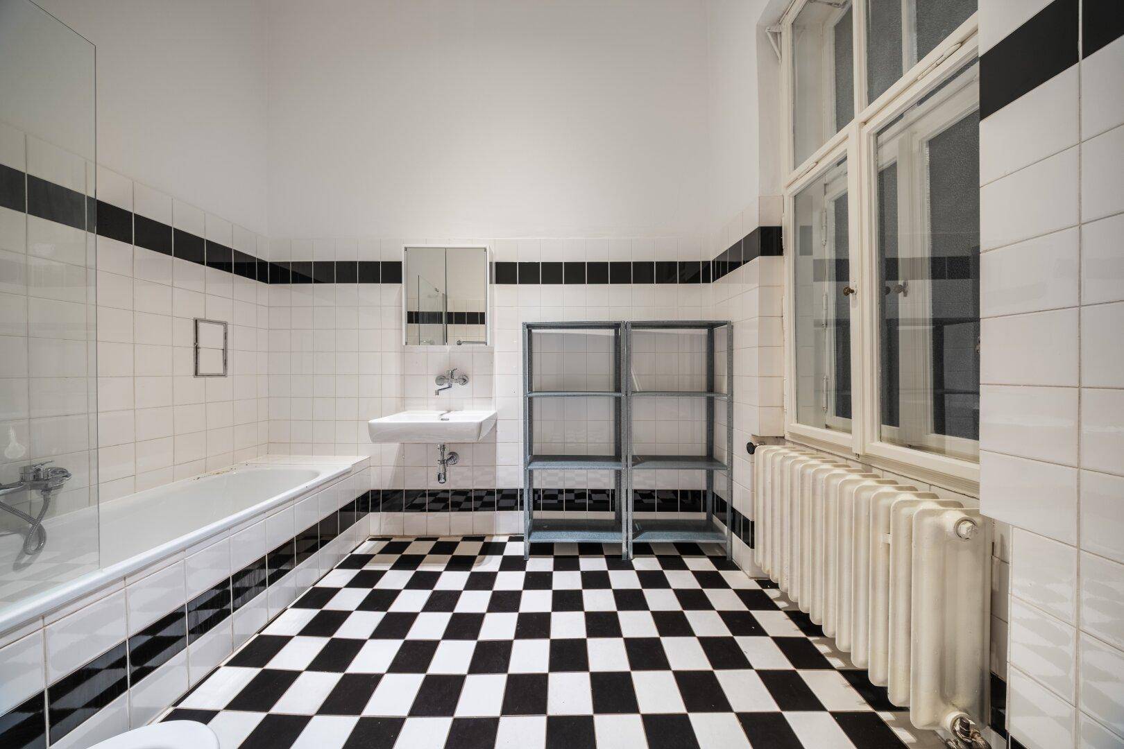 Badezimmer mit schwarz-weißem Schachbrettmuster-Fliesenboden, Badewanne und Fenster.