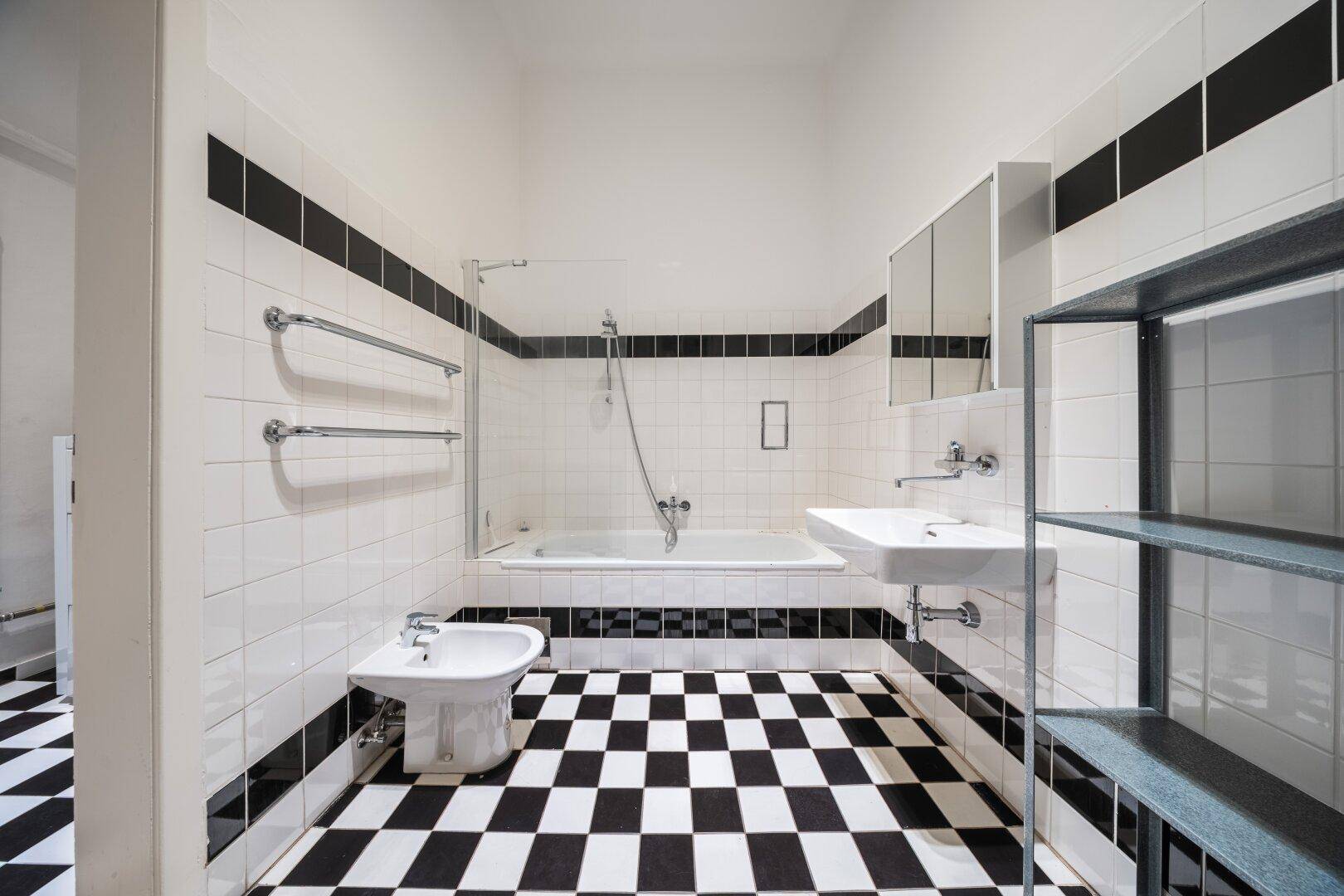 Helles Badezimmer mit Badewanne, Bidet, Waschbecken und markantem Fliesenmuster.