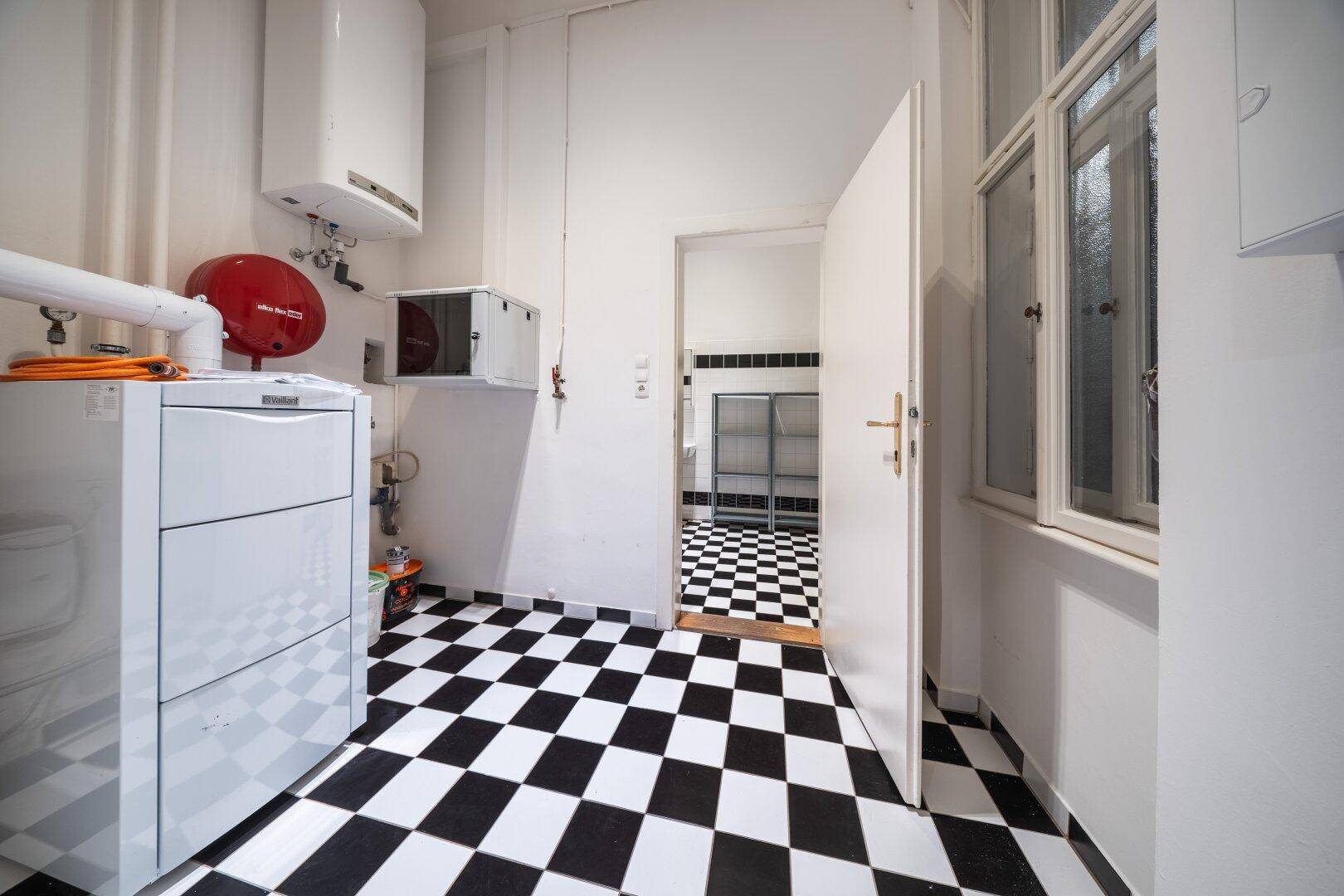 Hauswirtschaftsraum mit Heizungsanlage und schwarz-weißem Fliesenboden, angrenzend an ein Bad.