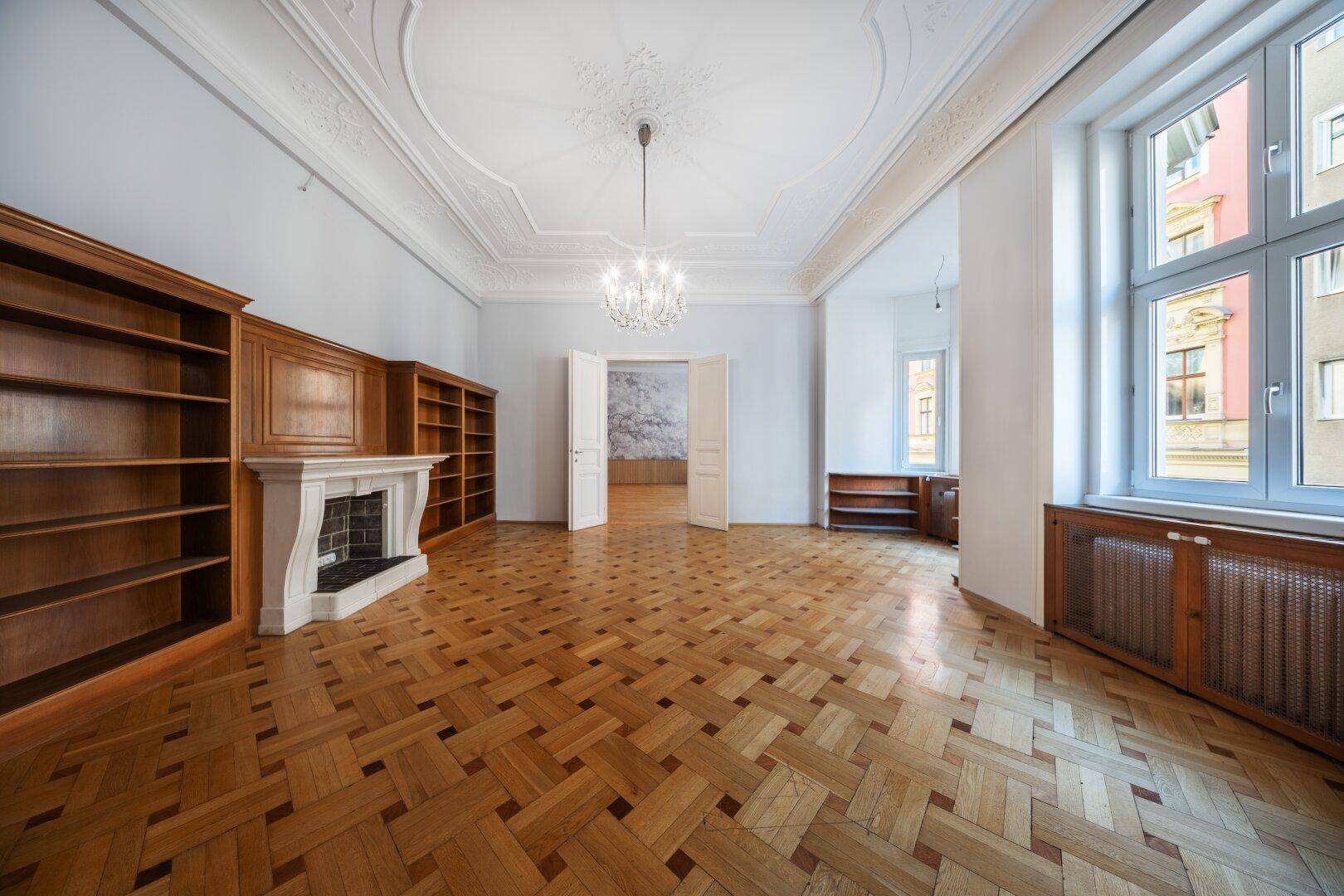Elegantes Wohnzimmer mit Fischgrätparkett, Kamin, Bücherregalen und Stuckdecke.