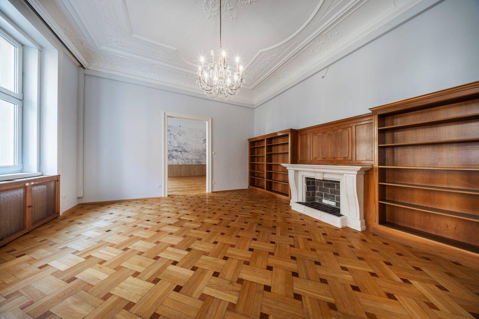 Klassisches Wohnzimmer mit Fischgrätparkett, Kamin, Bücherregalen und Kronleuchter.