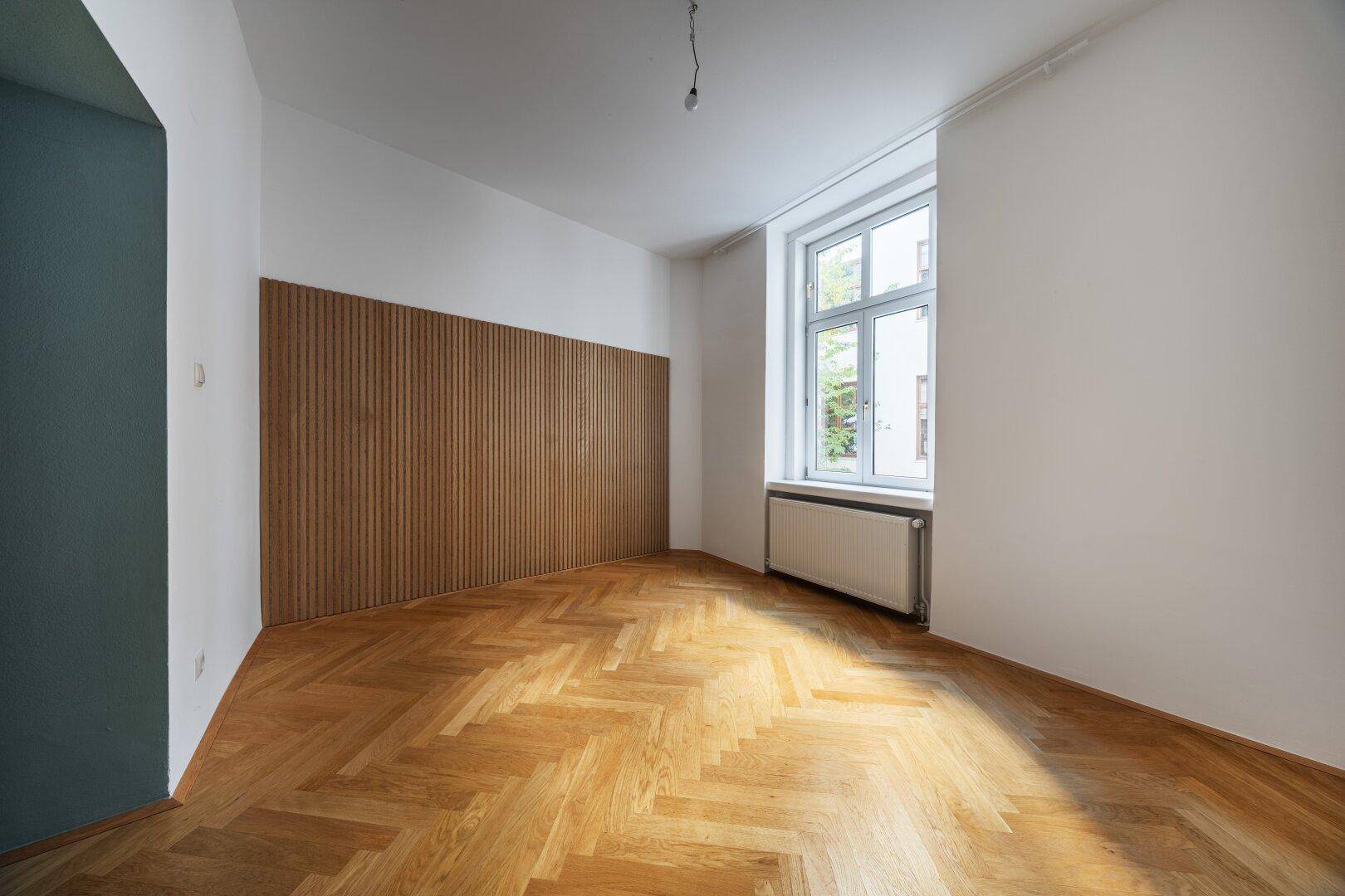 Heller Raum mit Fischgrätparkett, Holzwandverkleidung und großem Fenster.