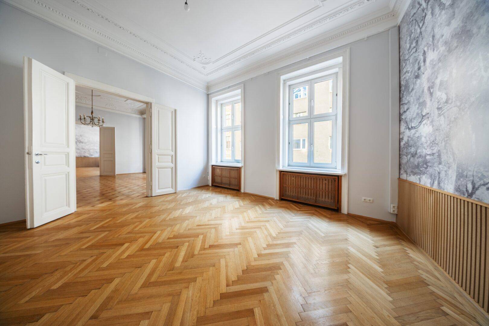 Heller Wohnraum mit Fischgrätparkett, Stuckdecke und dekorativer Wandgestaltung.