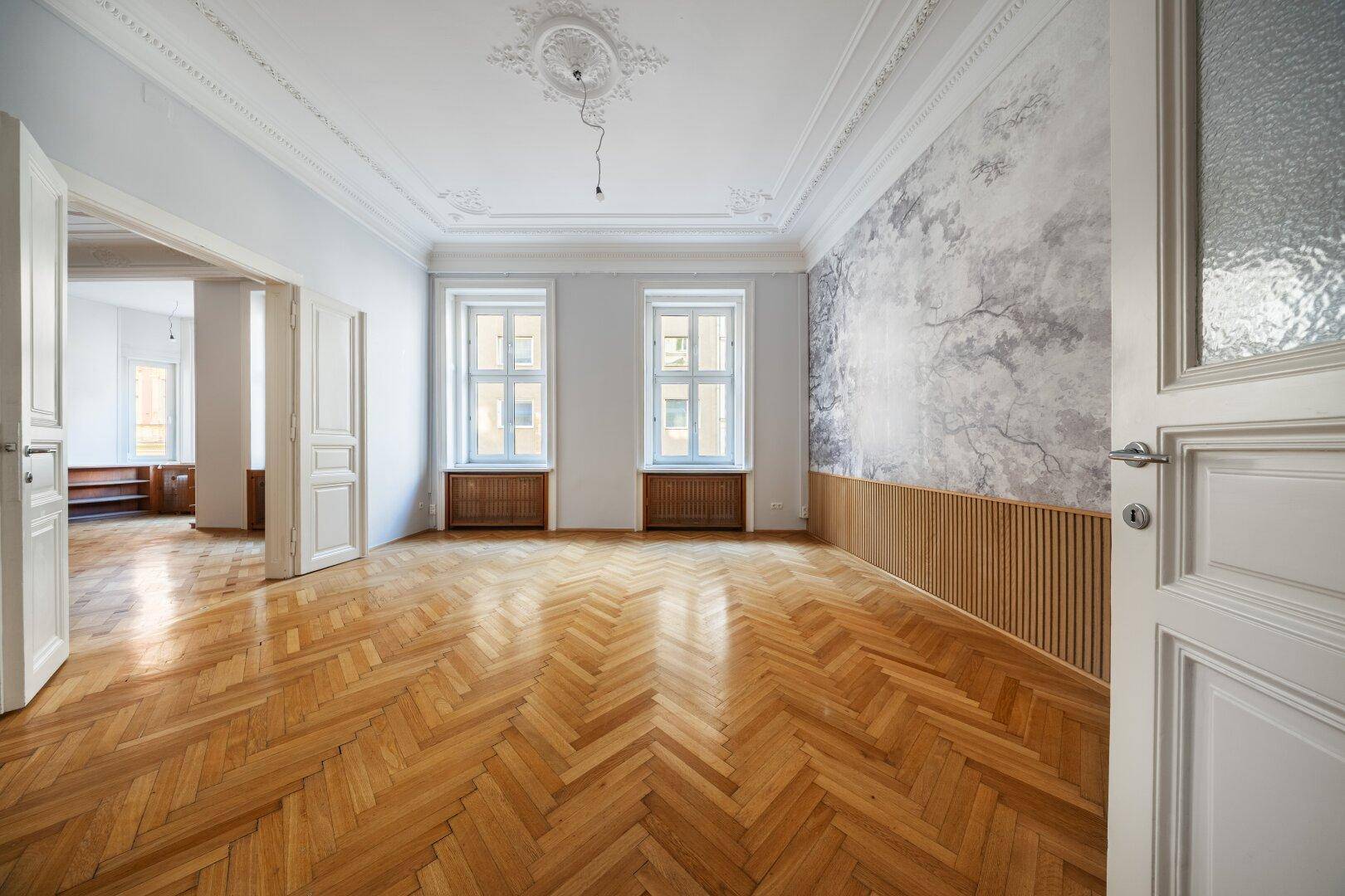 Helles Wohnzimmer mit Fischgrätparkett, Stuckdecke und dekorativer Wandgestaltung.