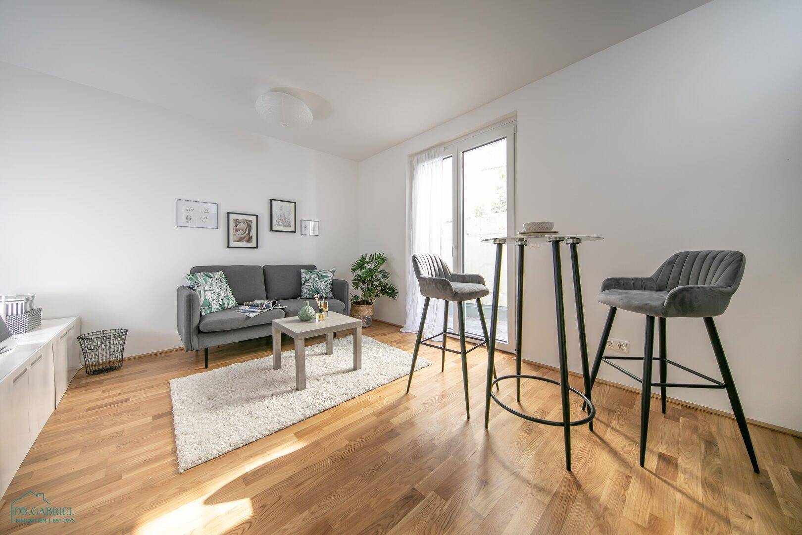 Freundliches Wohnzimmer mit bequemer Couch, Parkettboden und Zugang zu einem Außenbereich.