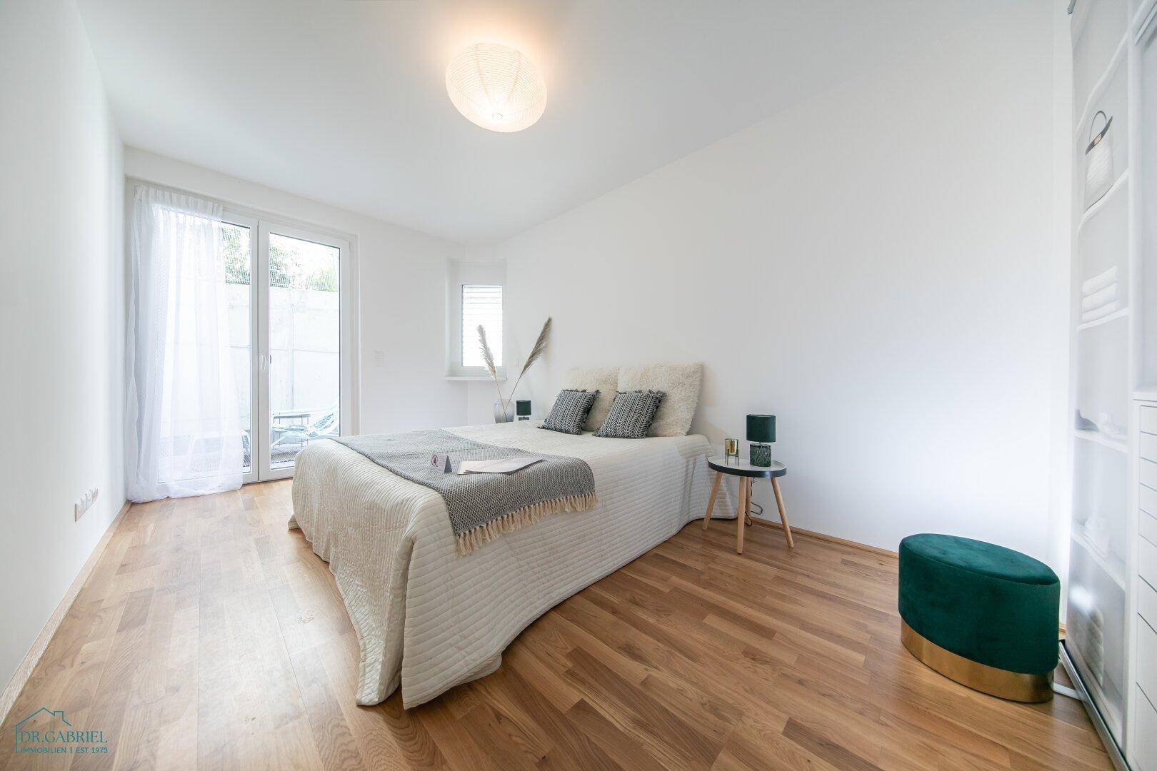 Helles Schlafzimmer mit Doppelbett, Holzboden und direktem Zugang zu einem Außenbereich.