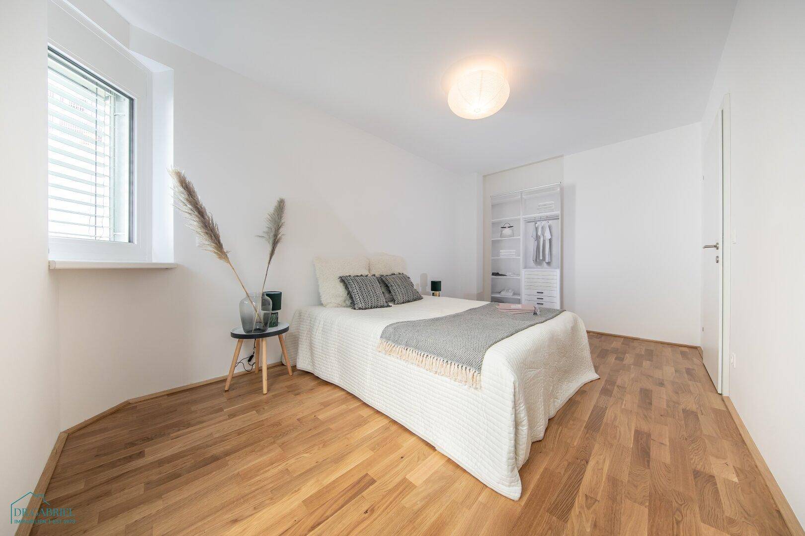Gemütliches Schlafzimmer mit Parkettboden, Fenster und offenem Kleiderschrank.