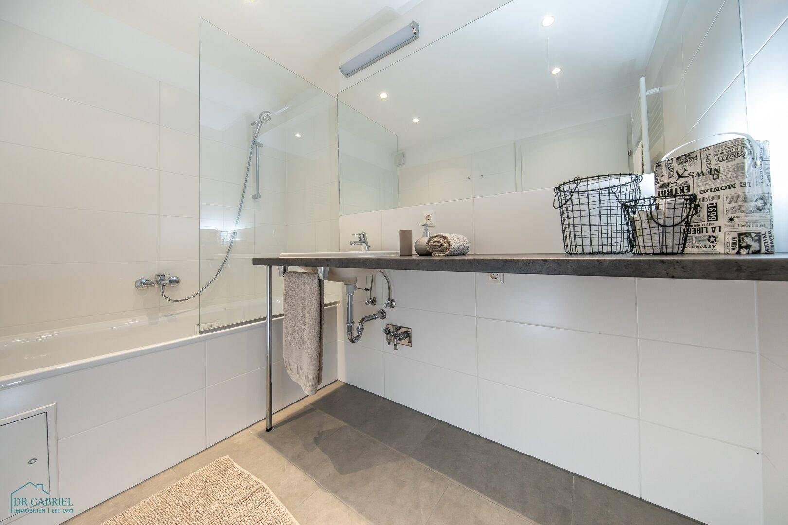 Modernes Badezimmer mit Badewanne, Duschwand und großem Spiegel über dem Waschbecken.