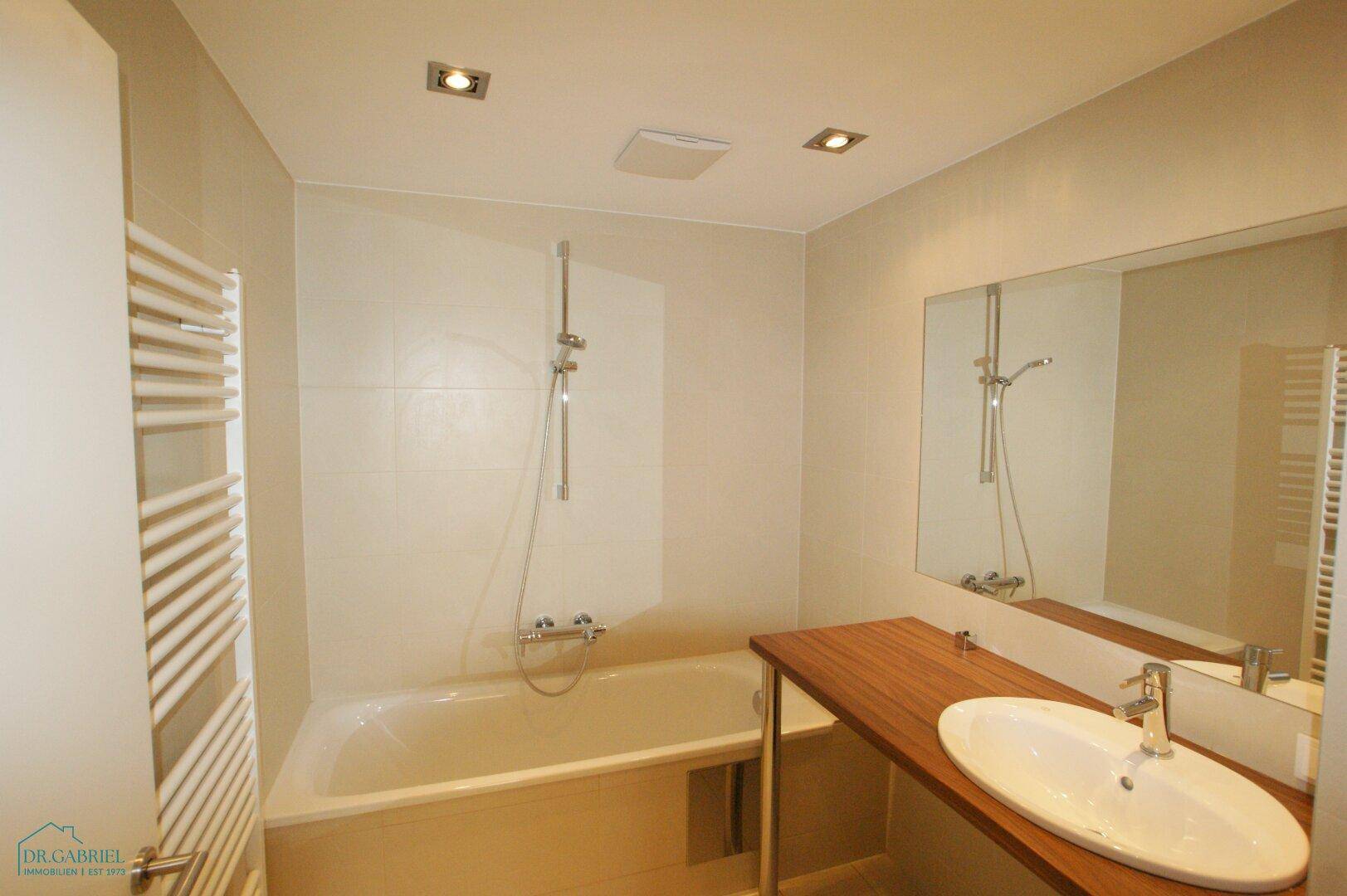 Modernes Badezimmer mit Badewanne, Duschvorrichtung, Einzelwaschbecken und beheiztem Handtuchhalter.