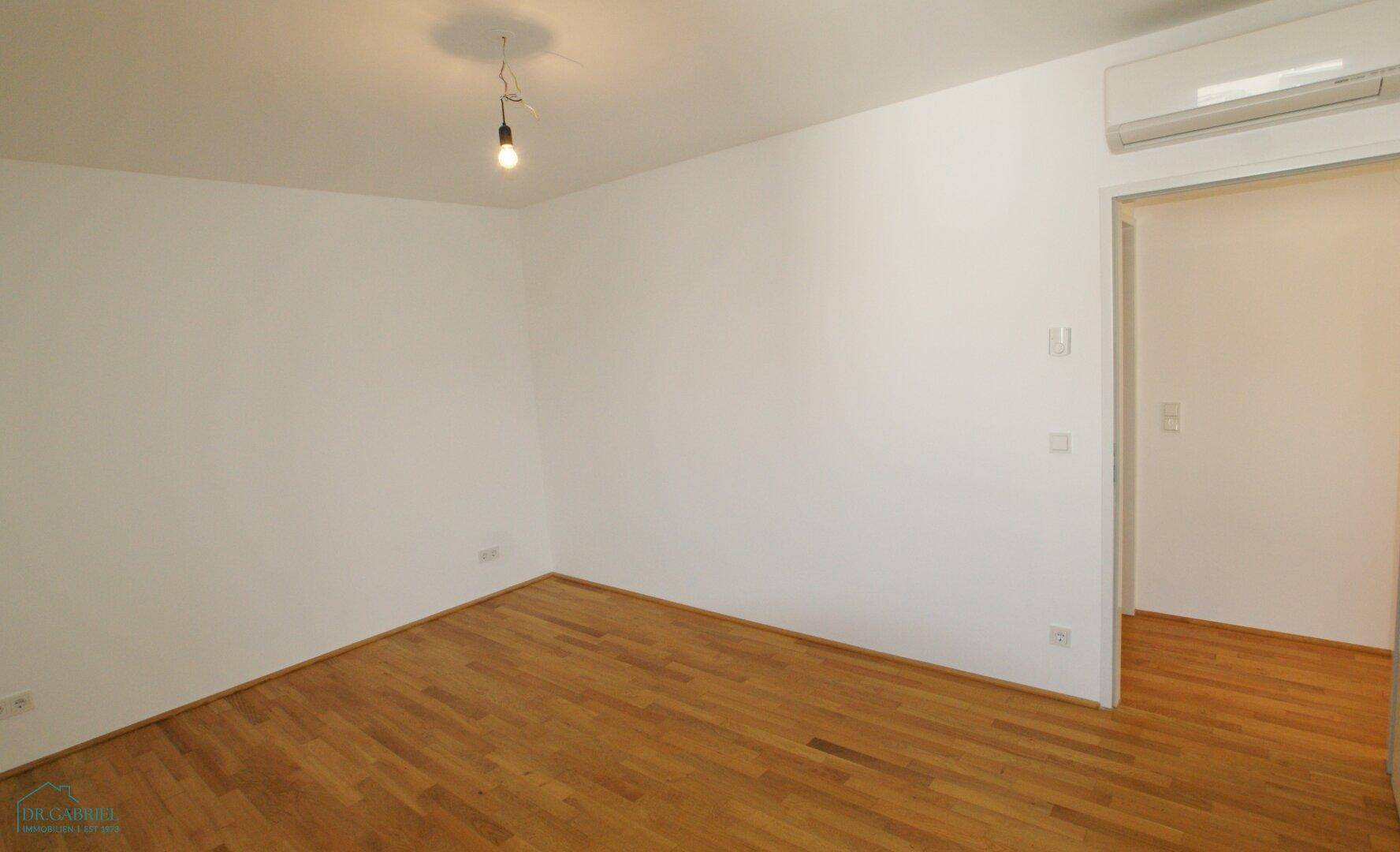 Helles, unmöbliertes Zimmer mit Holzboden und Klimaanlage, ideal als Schlafzimmer.