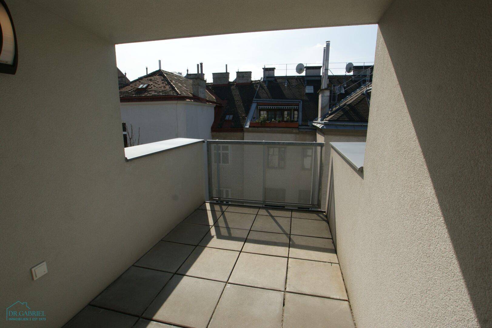 Heller, unmöblierter Balkon mit Fliesenboden und Blick auf die umliegenden Dächer.