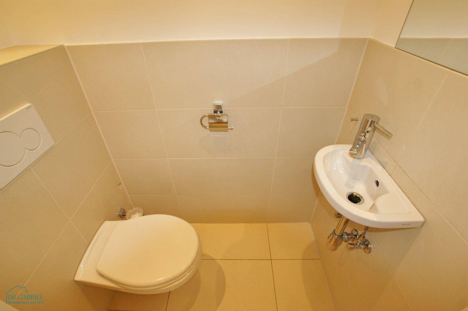 Kleines Gäste-WC mit Wand-WC und Handwaschbecken, hell gefliest.