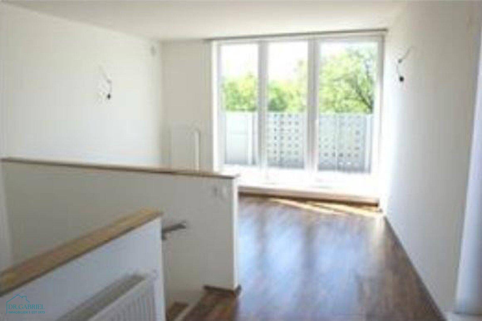 Heller Wohnbereich im Obergeschoss mit Parkettboden und Zugang zu einem Balkon.