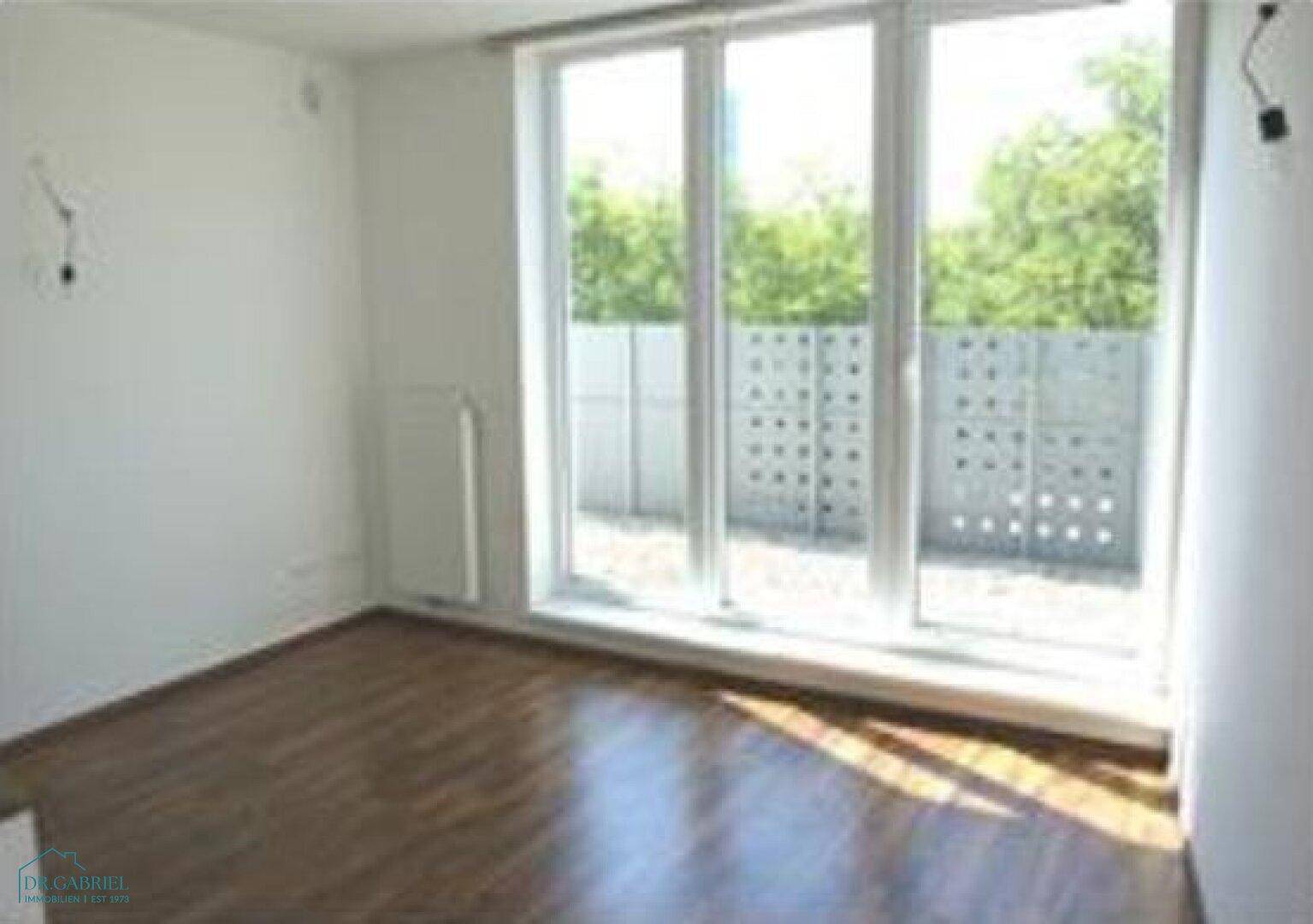 Helles Zimmer mit Parkettboden und großen Fenstern, die viel Tageslicht hereinlassen.