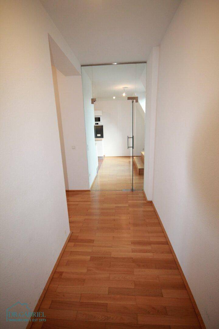 Heller Flur mit Holzparkettboden und einer modernen Glastür.