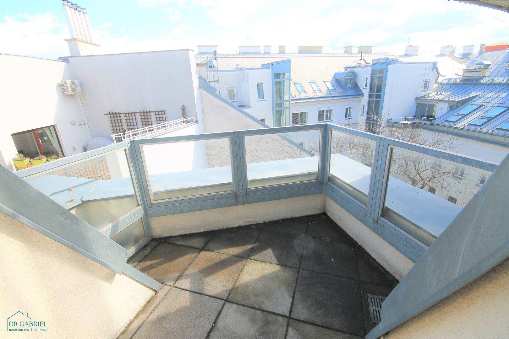 Sonniger Balkon mit Glasgeländer und Weitblick über die städtische Umgebung.