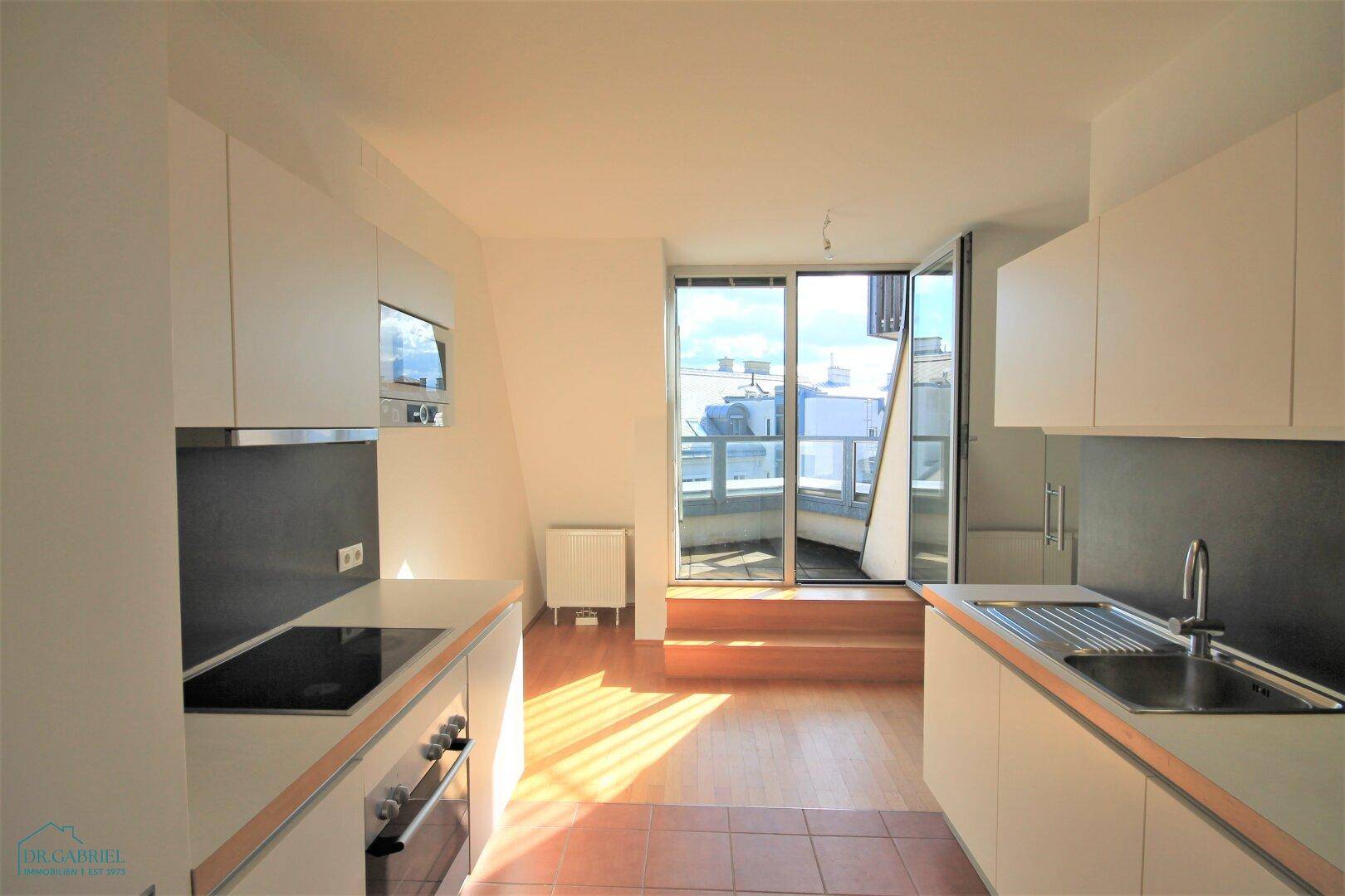 Moderne Küche mit weißen Schränken, integrierten Geräten und Zugang zum Balkon.