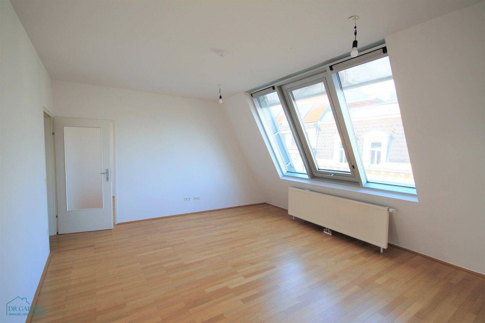 Geräumiges Wohnzimmer mit Dachschrägen, großen Fenstern und hellem Parkettboden.