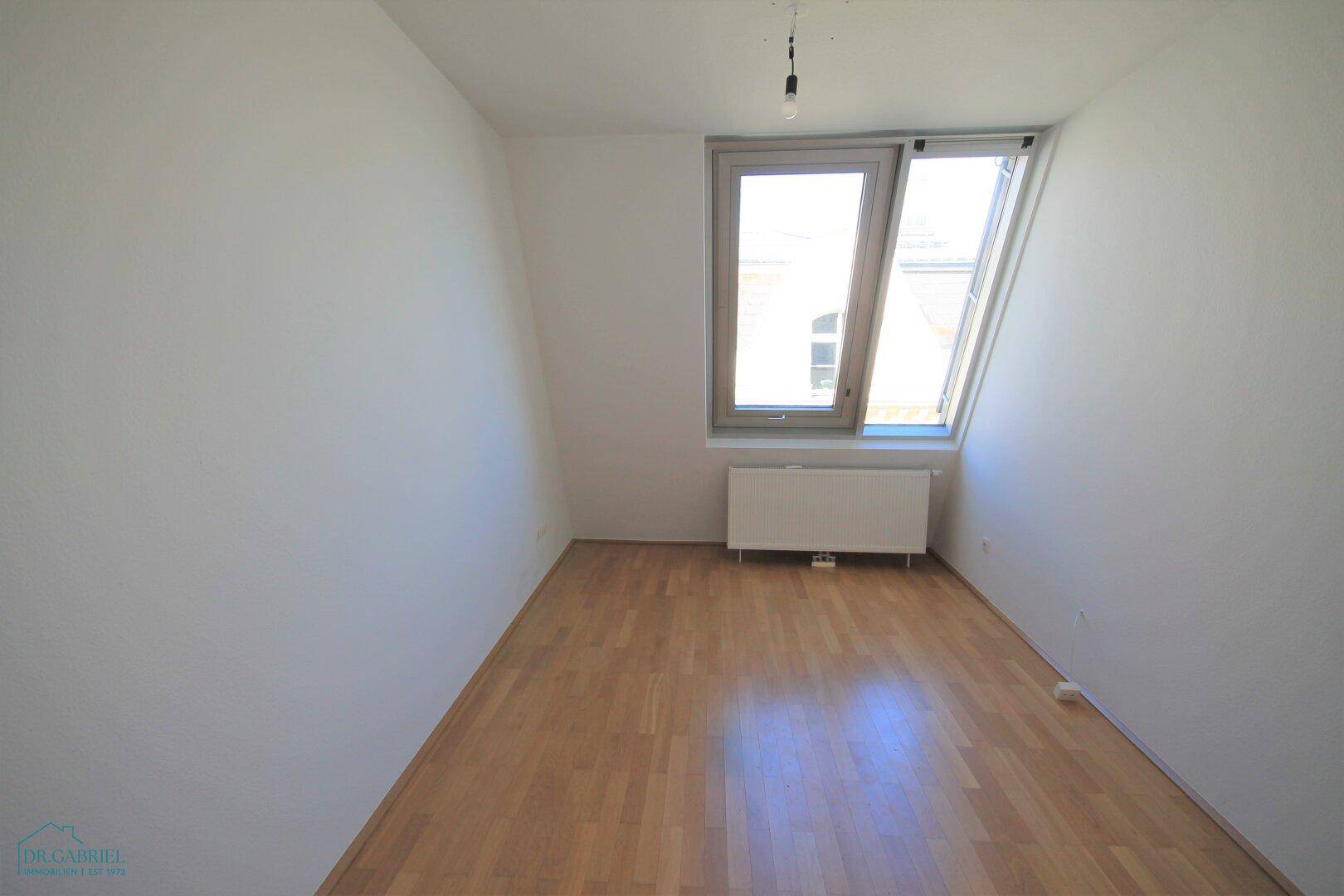Gemütliches Schlafzimmer mit Dachschräge, großem Fenster und hellem Parkettboden.