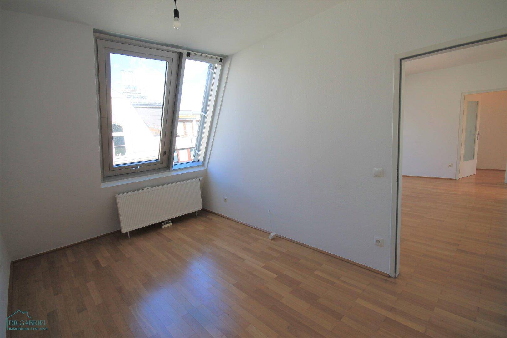 Helles Schlafzimmer mit schrägem Dachfenster und Zugang zu weiteren Räumen.