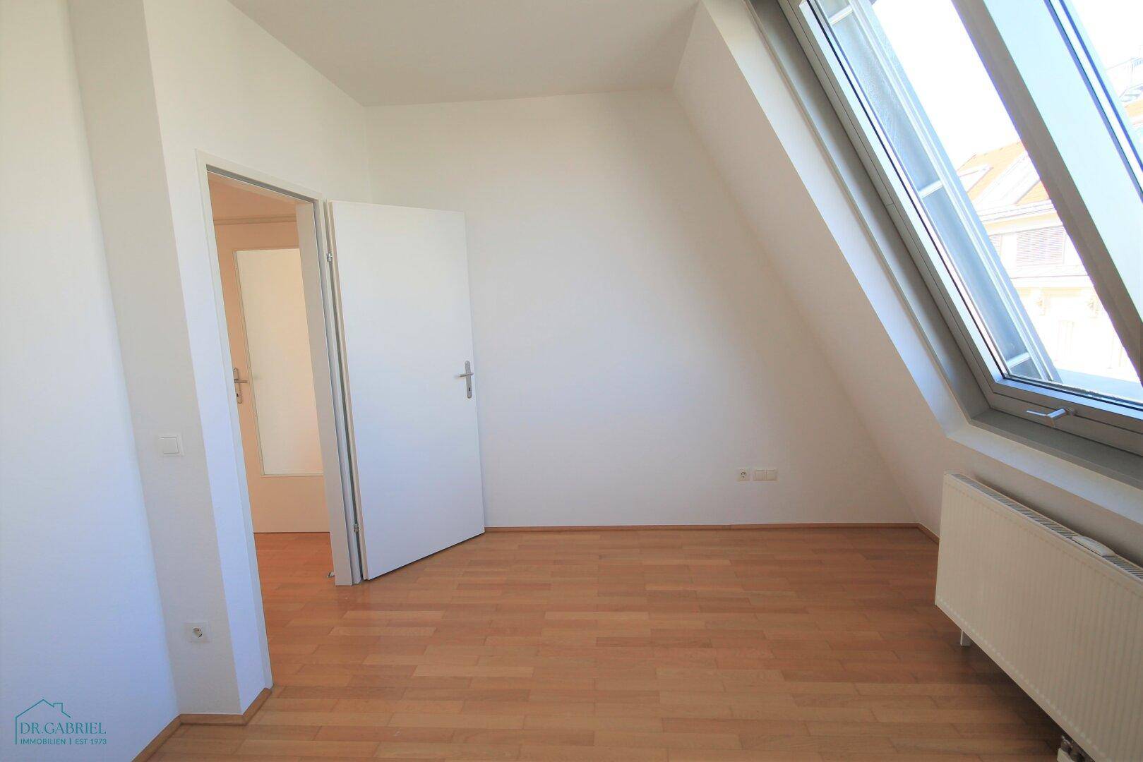 Geräumiges Schlafzimmer mit Dachschräge, Parkettboden und viel Tageslicht.