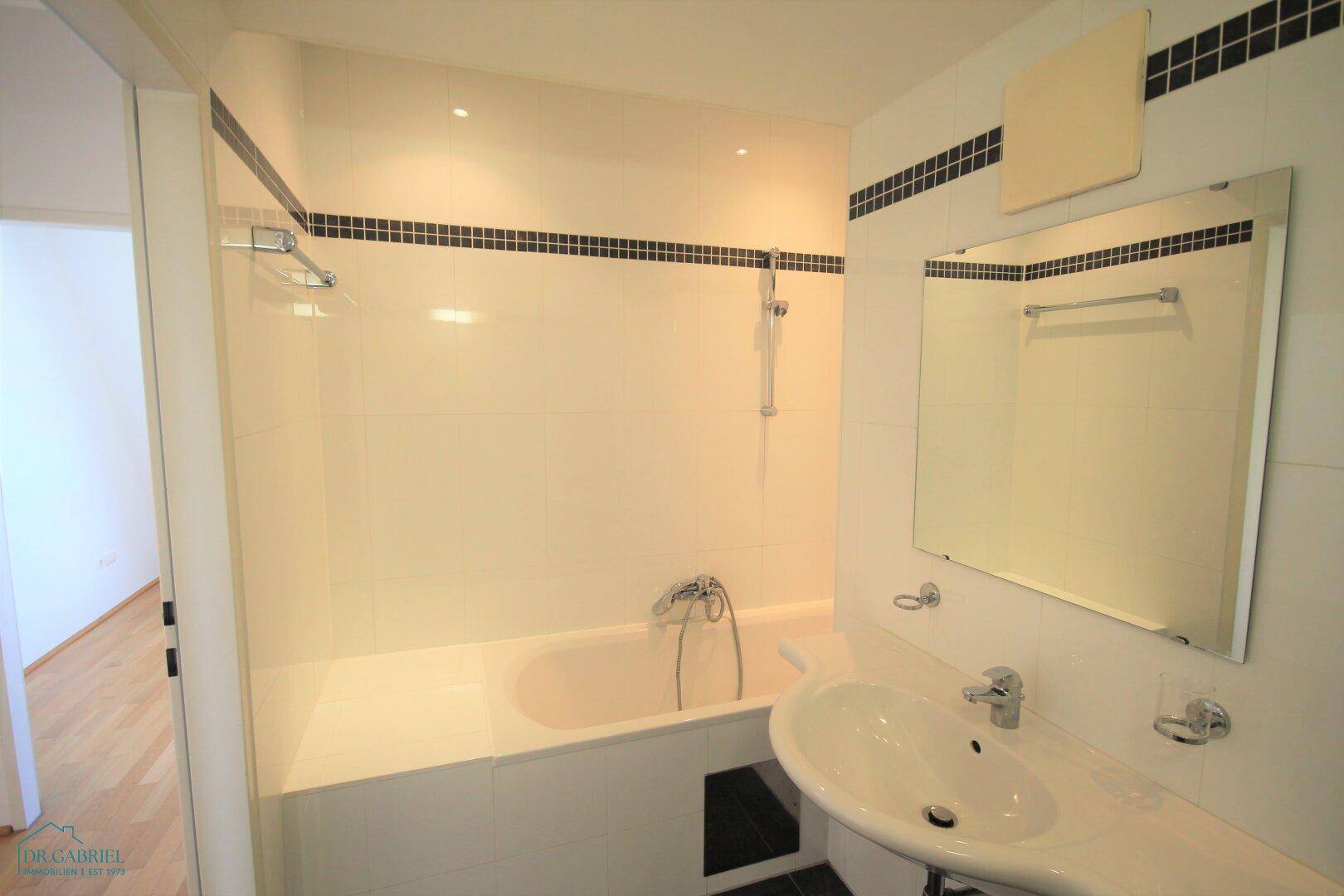 Funktionales Badezimmer mit Badewanne, Waschbecken und Spiegel, hell gefliest.