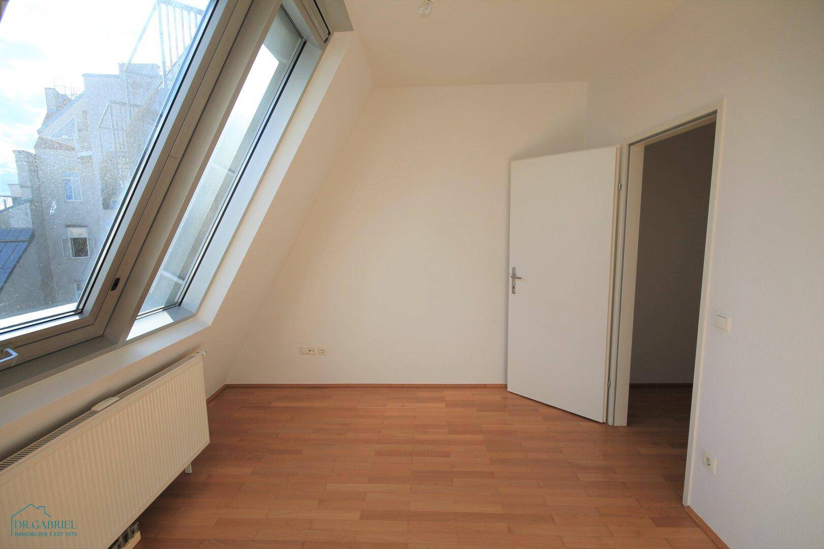 Schlafzimmer mit Dachschräge, hellem Parkett und großem Fenster für viel Licht.