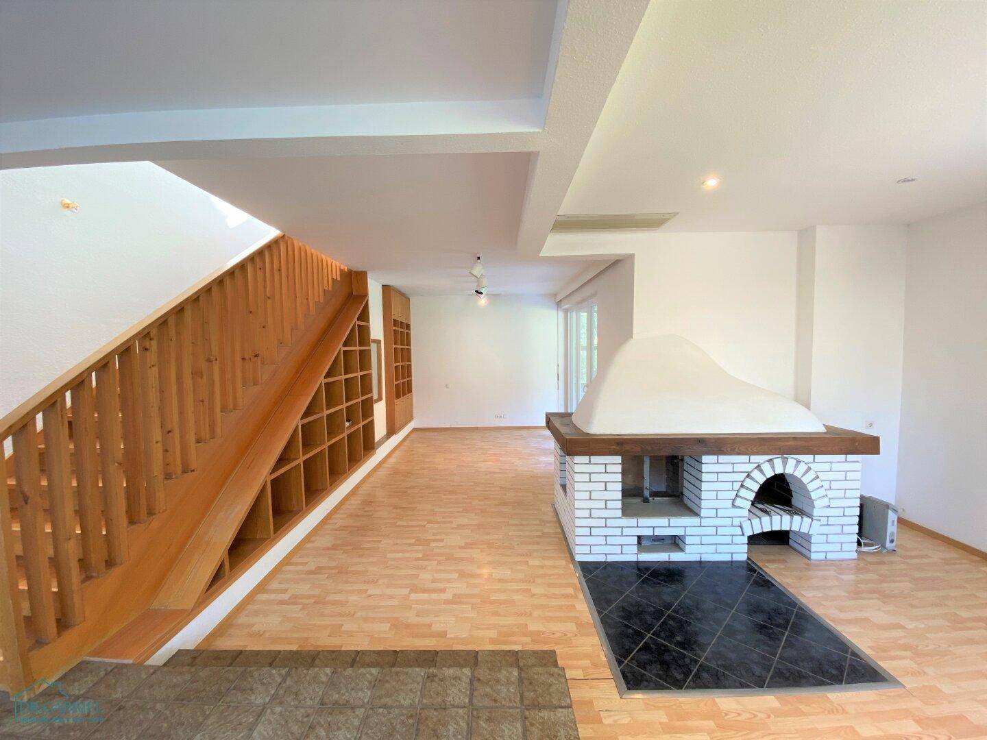 Heller Wohnbereich mit Kamin, Holztreppe und integrierten Regalen, ideal für gemütliche Abende.