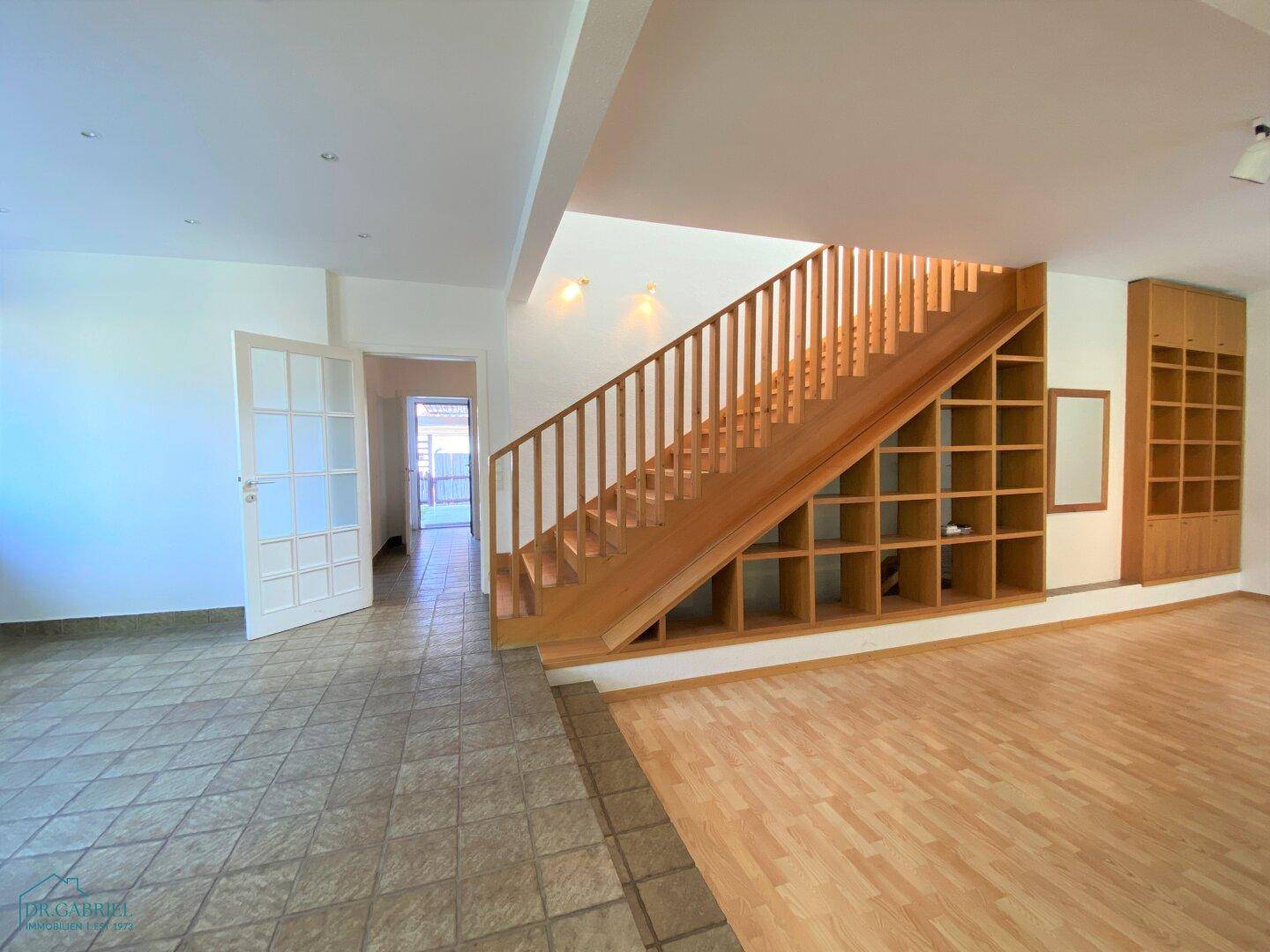Geräumiger Flur mit Fliesen- und Holzboden, der zu einer Holztreppe mit integrierten Regalen führt.