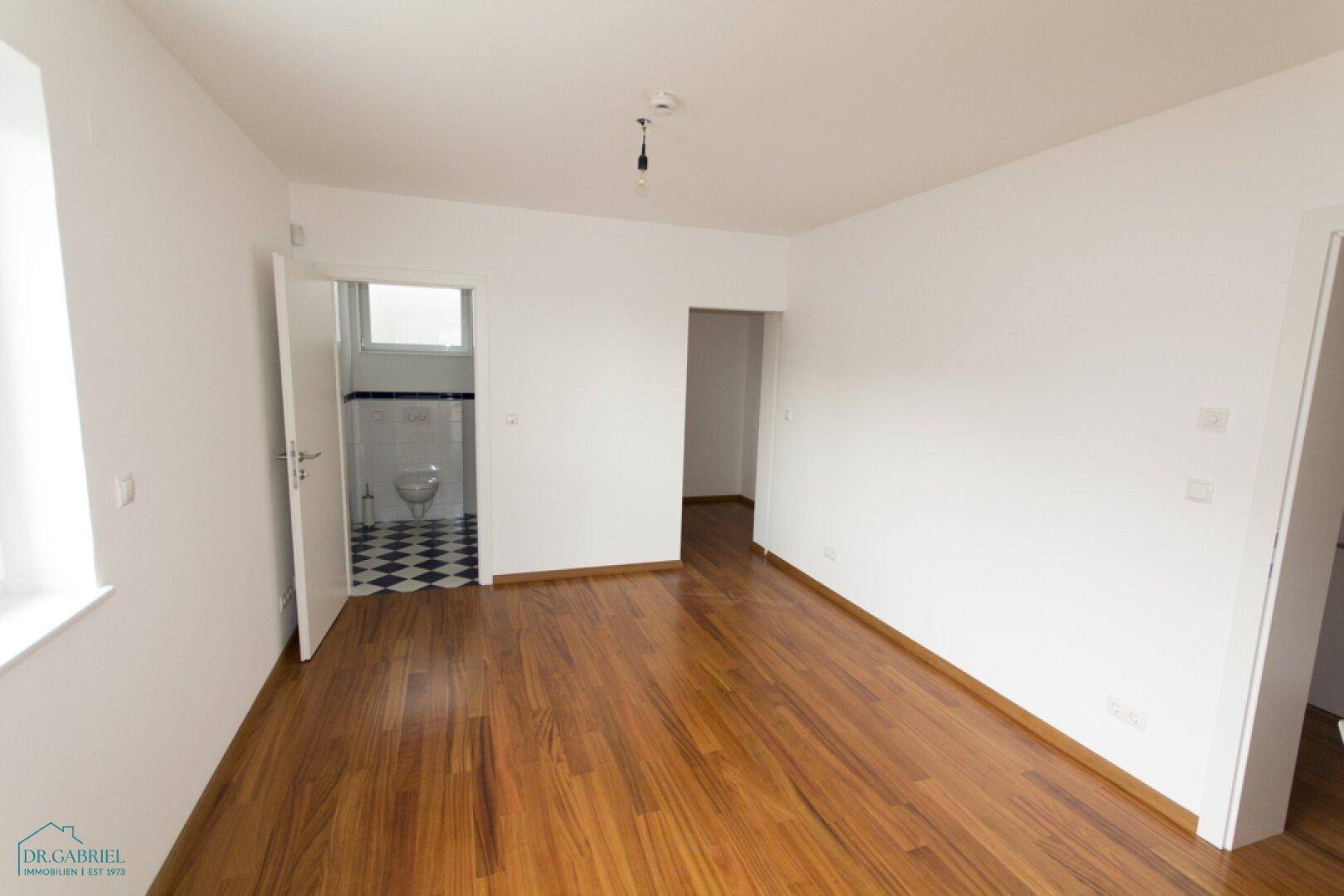 Schlafzimmer mit Holzboden und Zugang zu einem Badezimmer mit auffälligen schwarz-weißen Fliesen.