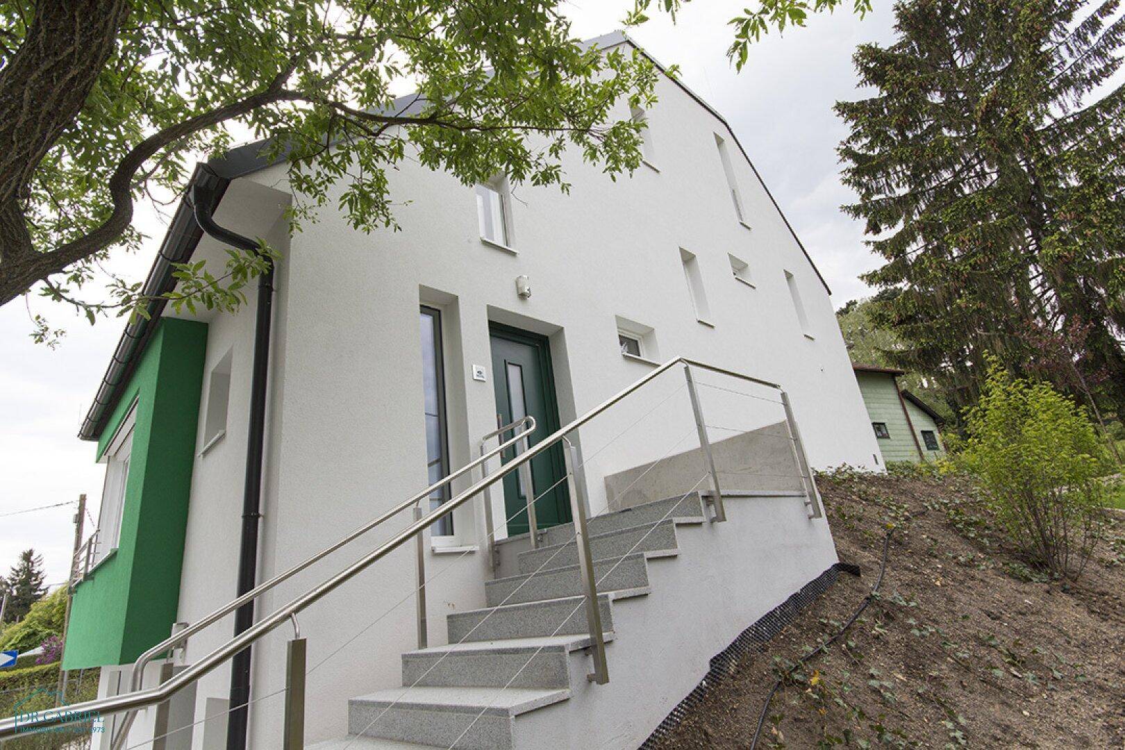 Eingangsbereich des modernen Hauses mit Treppe, grüner Tür und weißer Fassade.