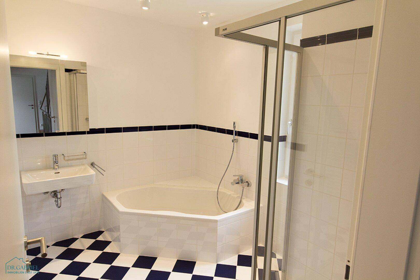 Badezimmer mit markanten schwarz-weißen Fliesen, Eckbadewanne, Duschkabine und Waschbecken.
