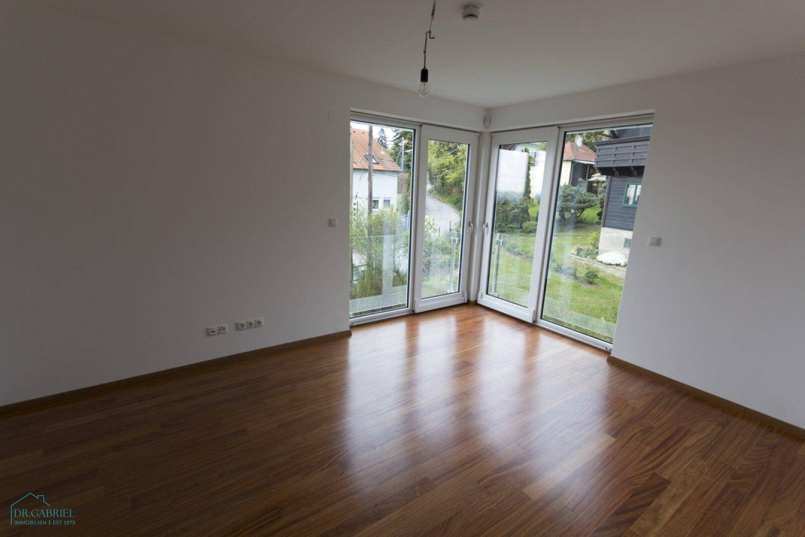 Heller Raum mit Holzboden und großen Eckfenstern, die einen weiten Blick auf die Umgebung bieten.