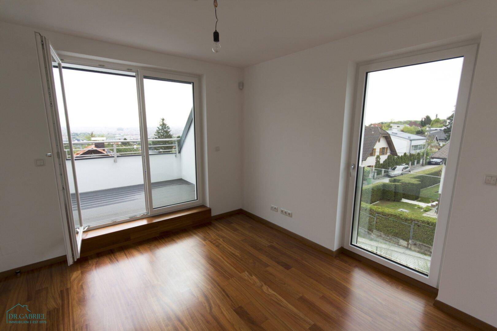 Schlafzimmer mit Holzboden und Zugang zu einem Balkon, der einen weiten Ausblick ermöglicht.