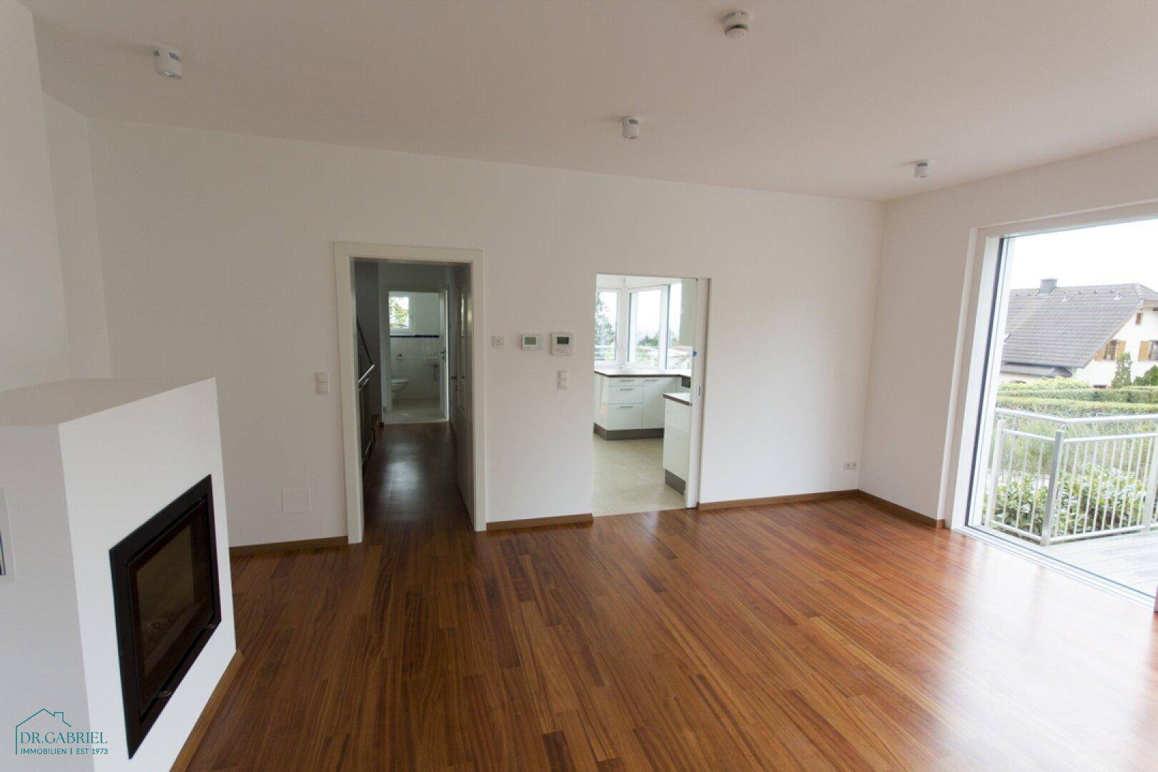 Wohnzimmer mit Holzboden und Kamin, mit Zugängen zu Küche und Badezimmer sowie Balkon.