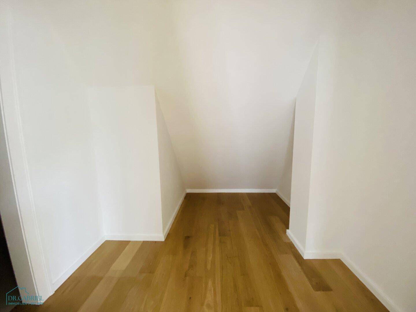 Kleiner Abstellraum mit Holzparkettboden und schrägen Wänden, ideal für zusätzlichen Stauraum.