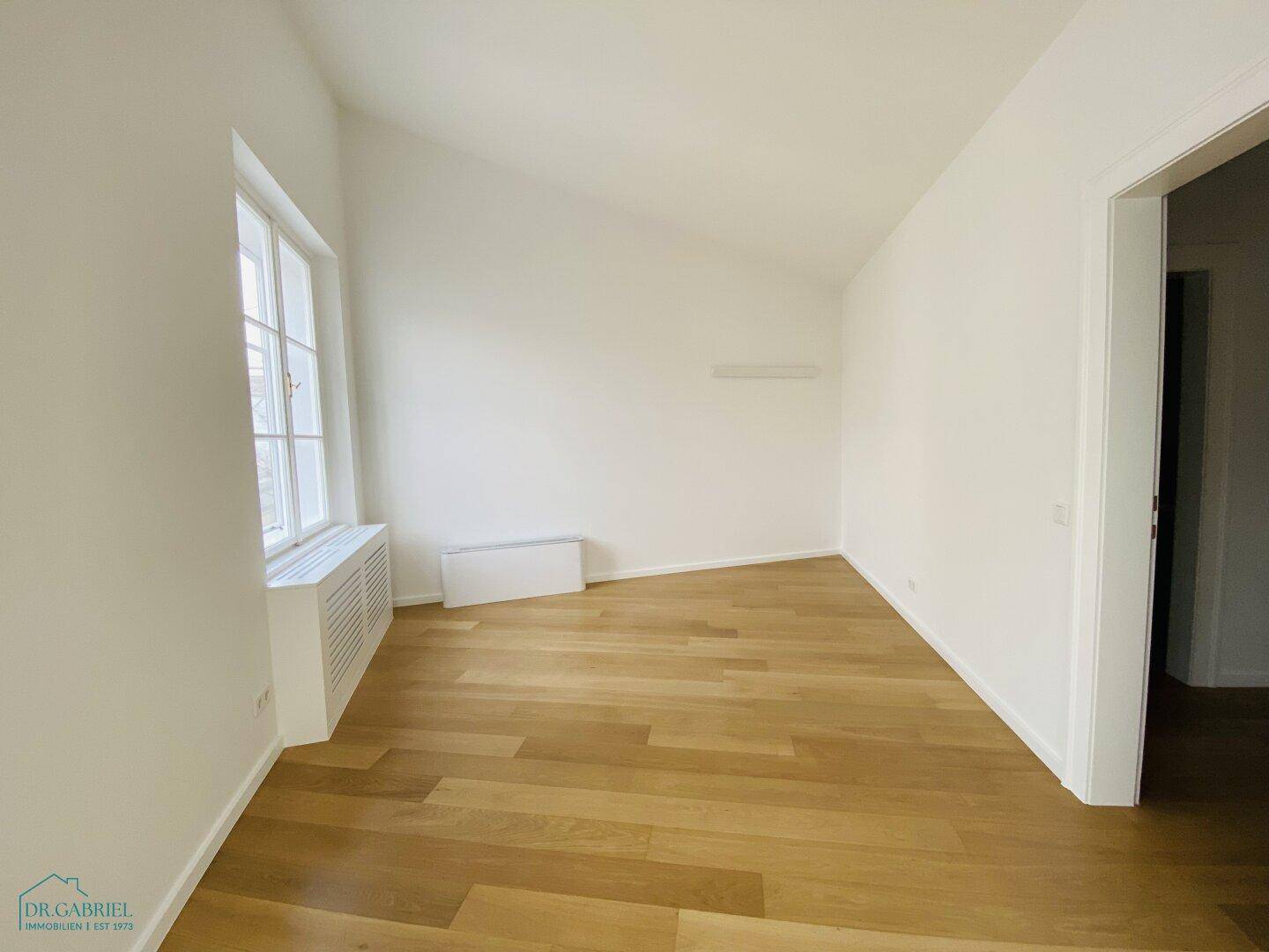 Geräumiges Zimmer mit Holzparkettboden, weißen Wänden und einem großen Fenster für viel Tageslicht.