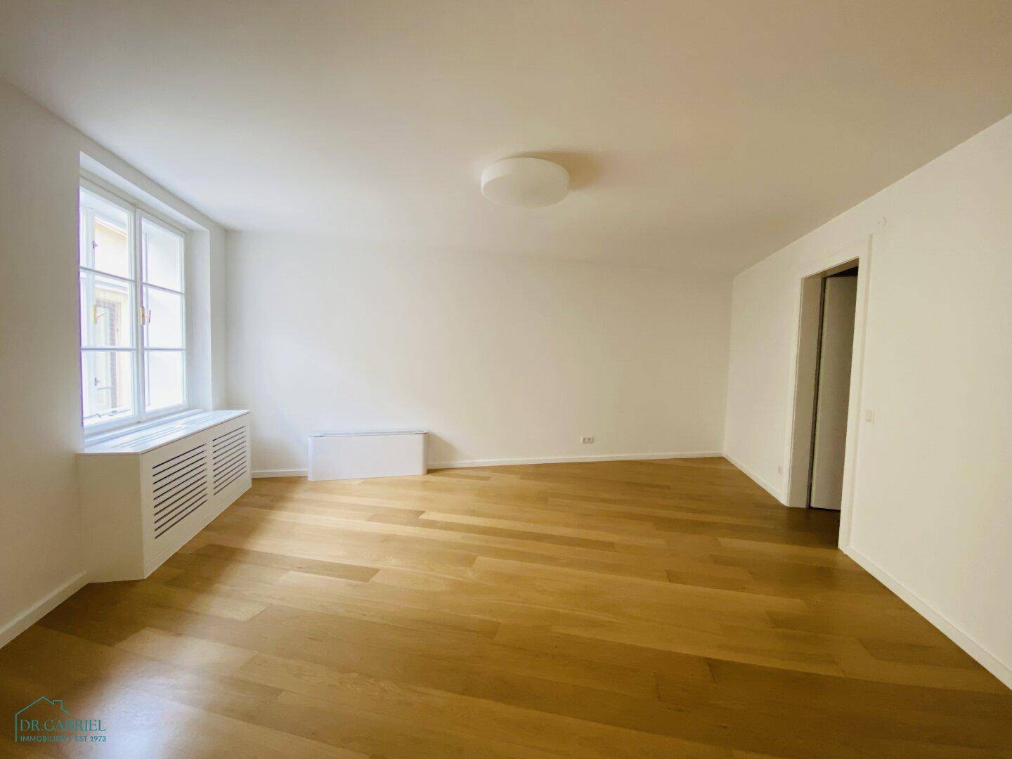 Geräumiges Zimmer mit Holzparkettboden, weißen Wänden und einem großen Fenster für viel Tageslicht.