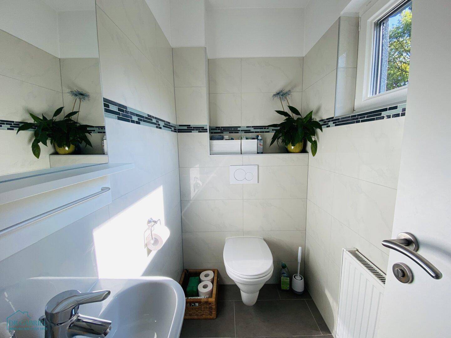 Modernes Gäste-WC mit Waschbecken, wandhängendem WC und Fenster für Tageslicht.
