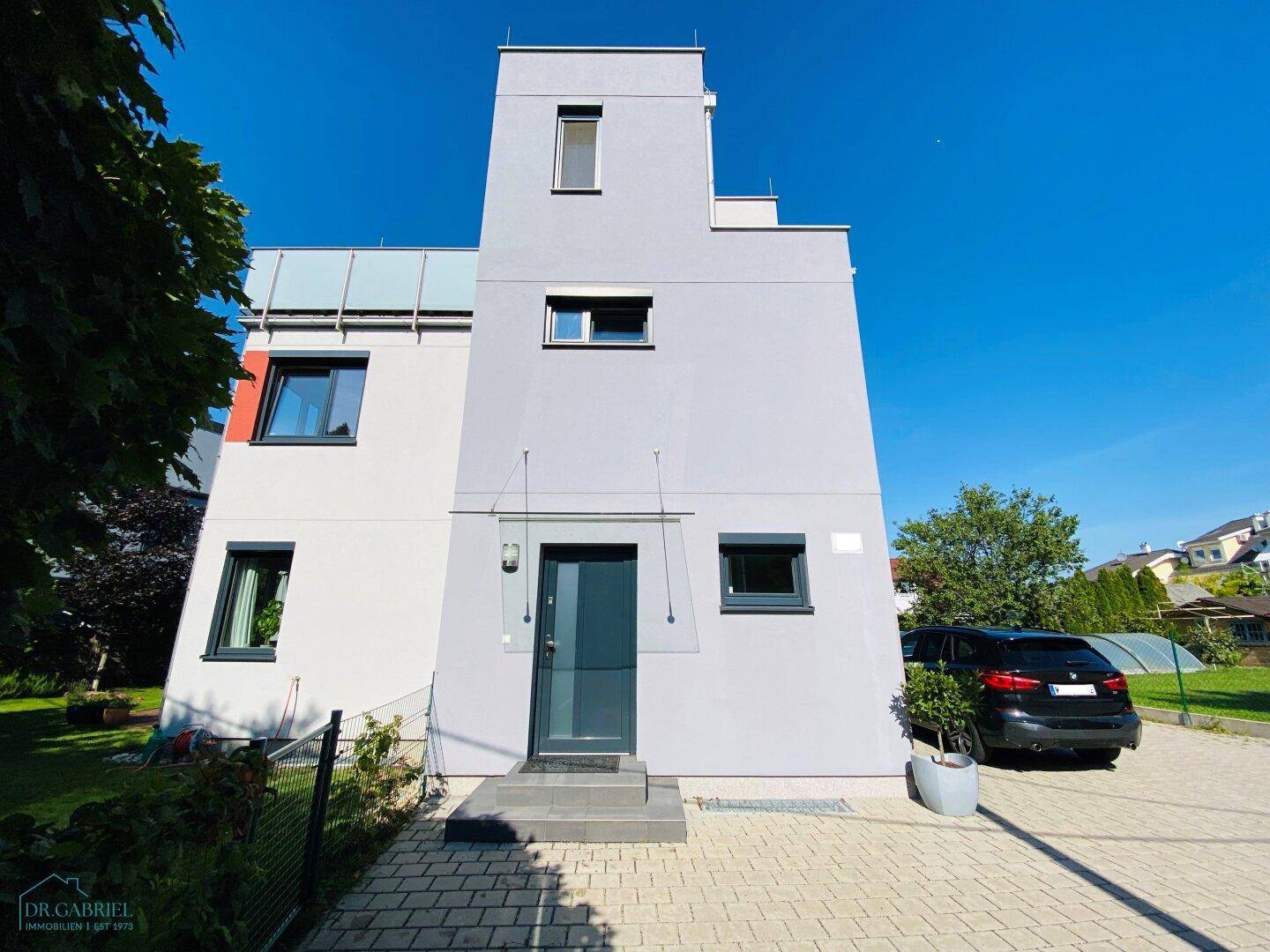 Vorderansicht des modernen Gebäudes mit gepflasterter Zufahrt und gepflegtem Vorgarten.