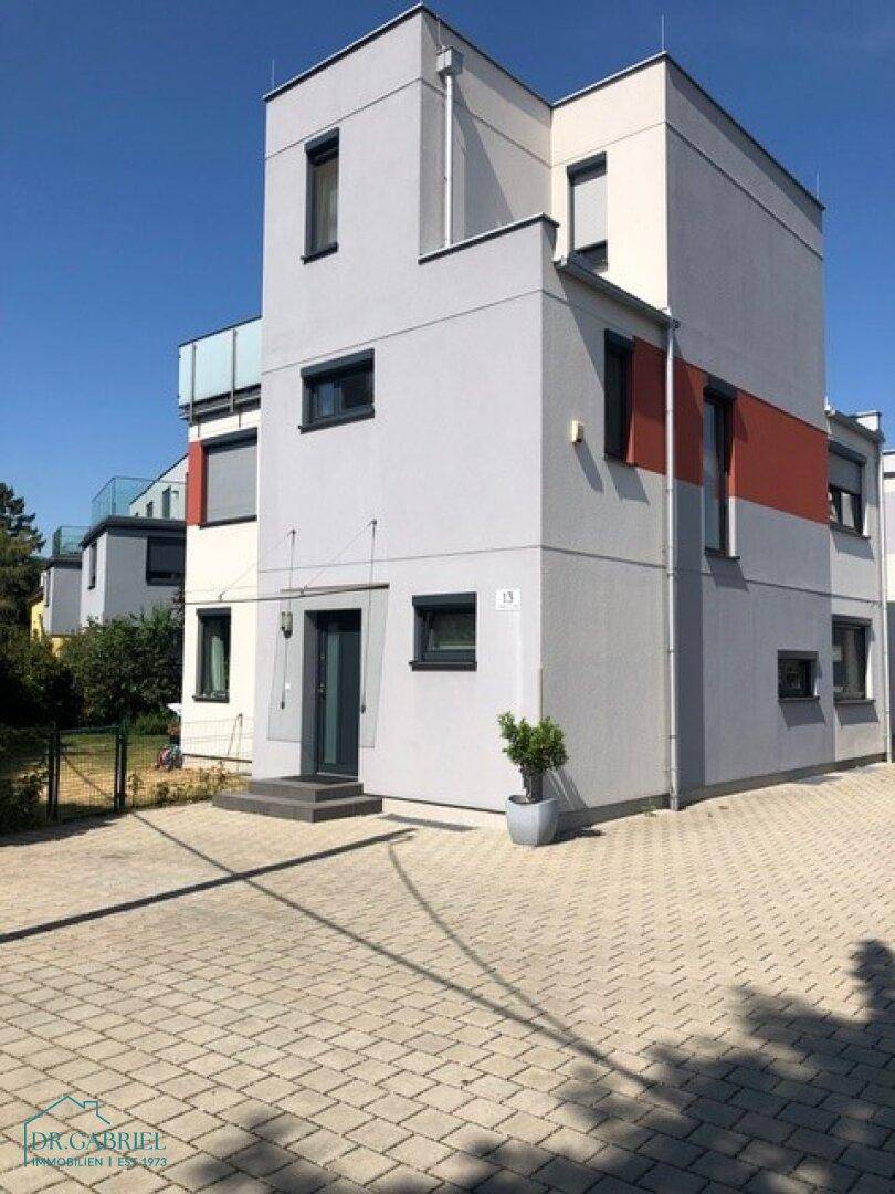 Moderne Gebäudefassade mit grauen und roten Akzenten und gepflasterter Zufahrt.
